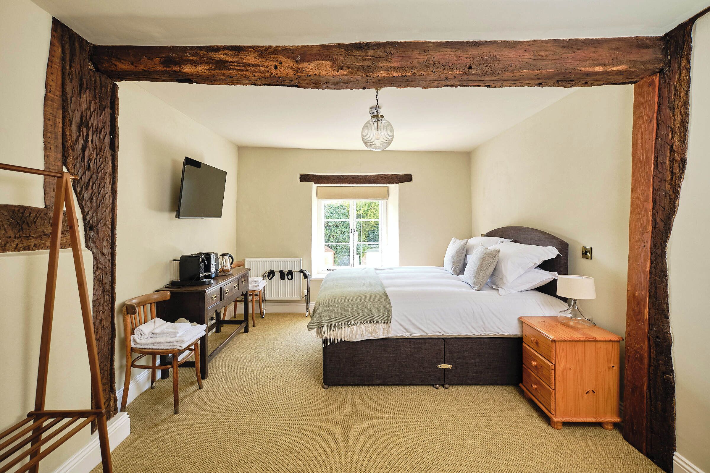 Une chambre avec un plafond en bois, un lit avec des oreillers, une table de chevet, un bureau avec une chaise et un radiateur.