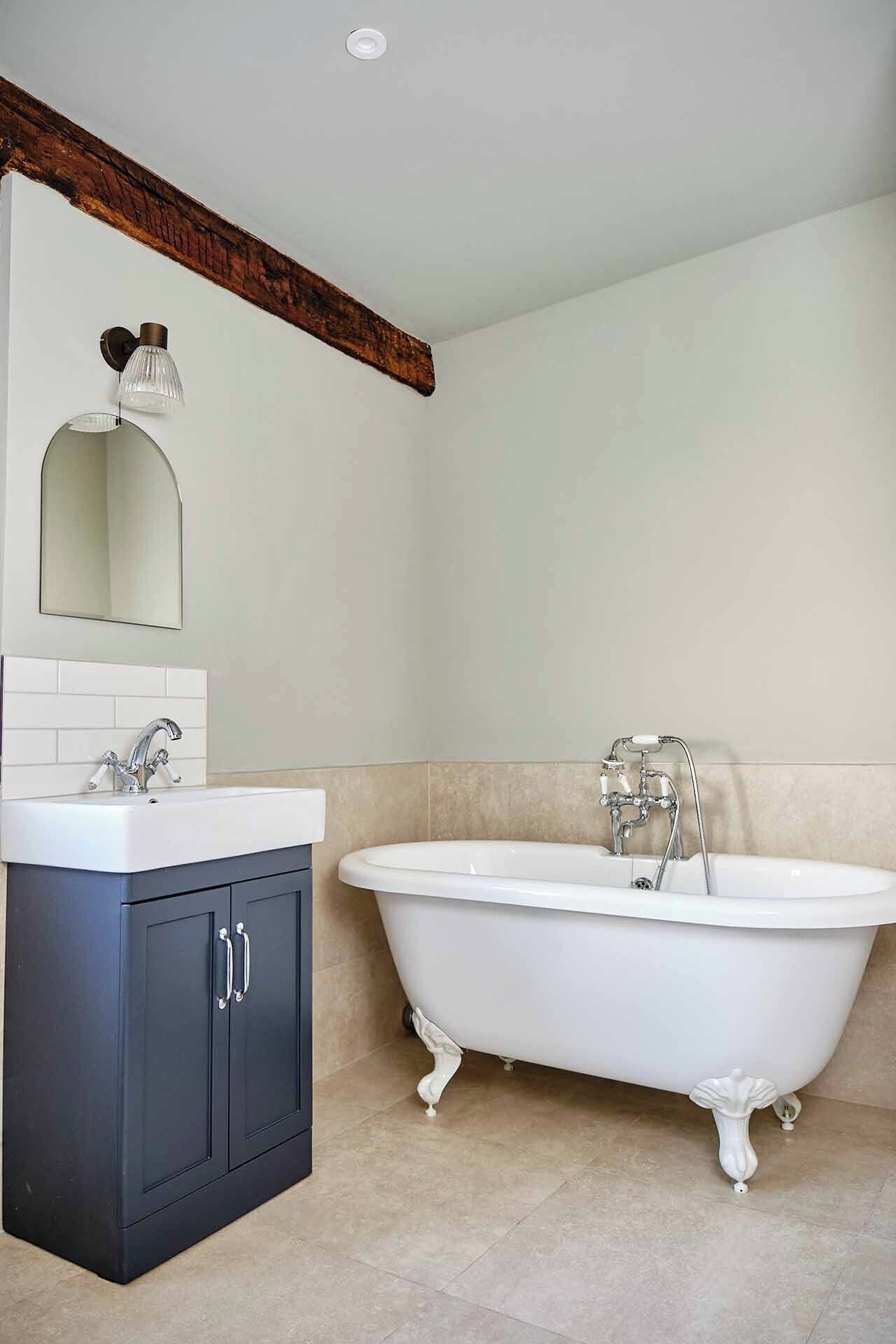 Une salle de bain avec une baignoire sur pieds, un meuble-lavabo avec un miroir et un luminaire placé au-dessus du miroir.