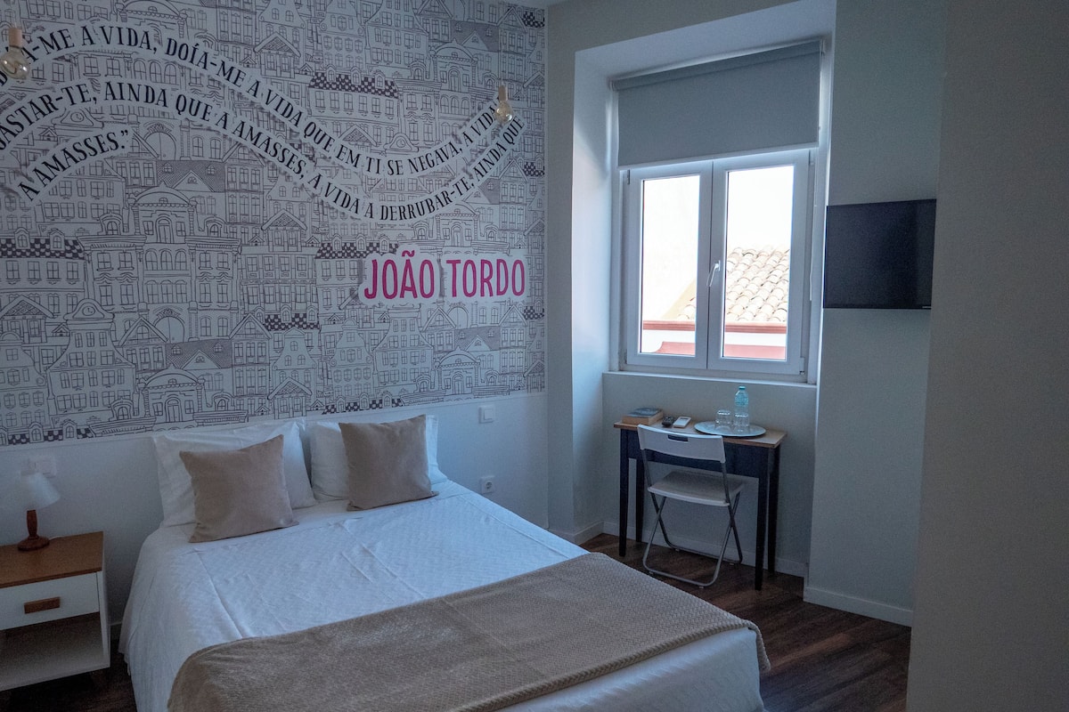 A bedroom with a bed, a desk, and a window.