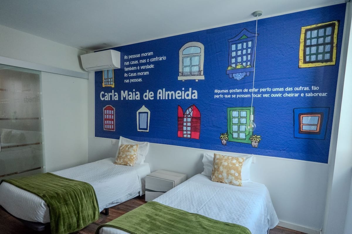 A hotel room with two beds, a large wall mural with text and window illustrations, and a glass door closet.