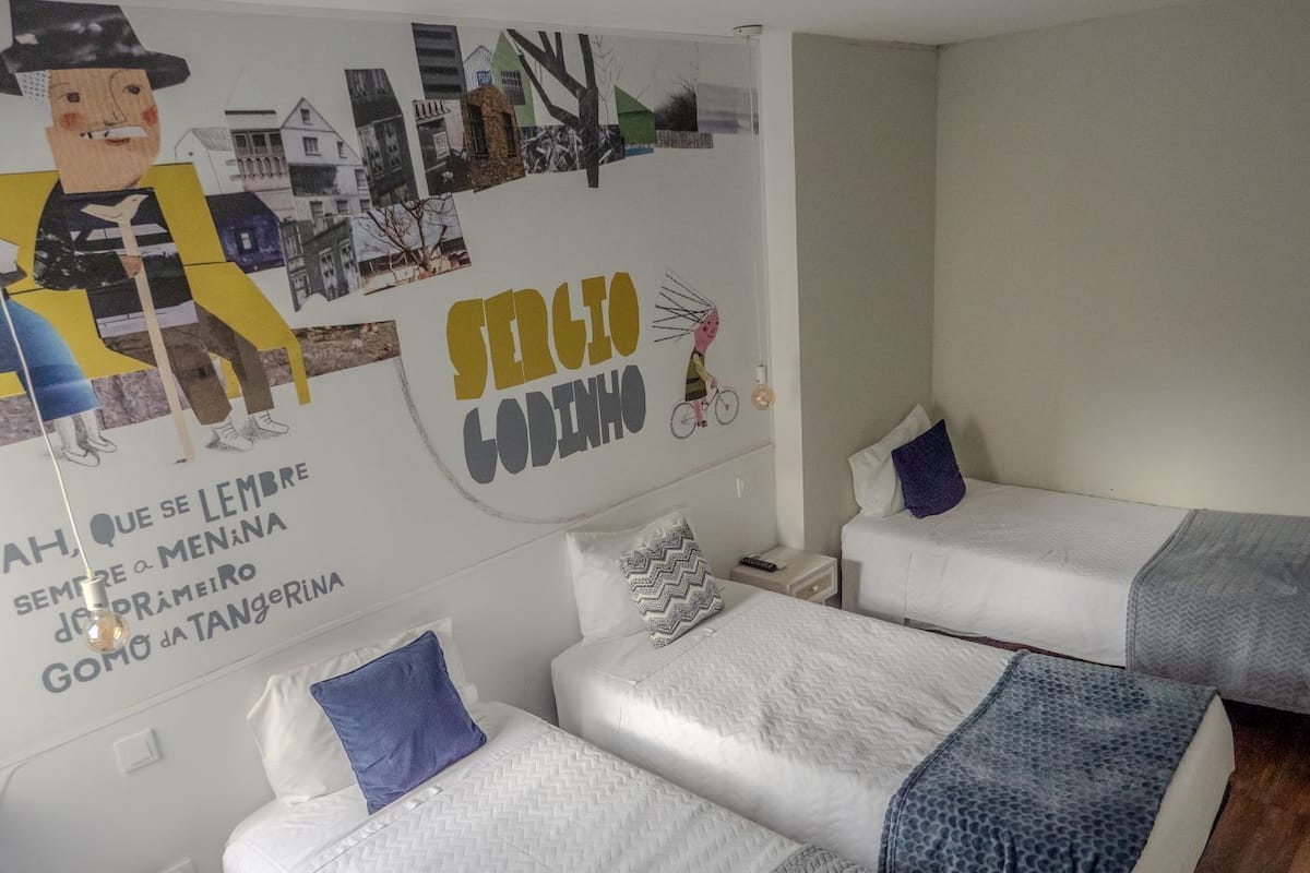 A hotel room with three single beds, a small bedside table, and a wall mural.