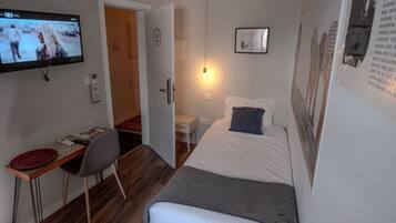 Quarto pequeno e moderno com uma cama, uma escrivaninha e uma televisão.