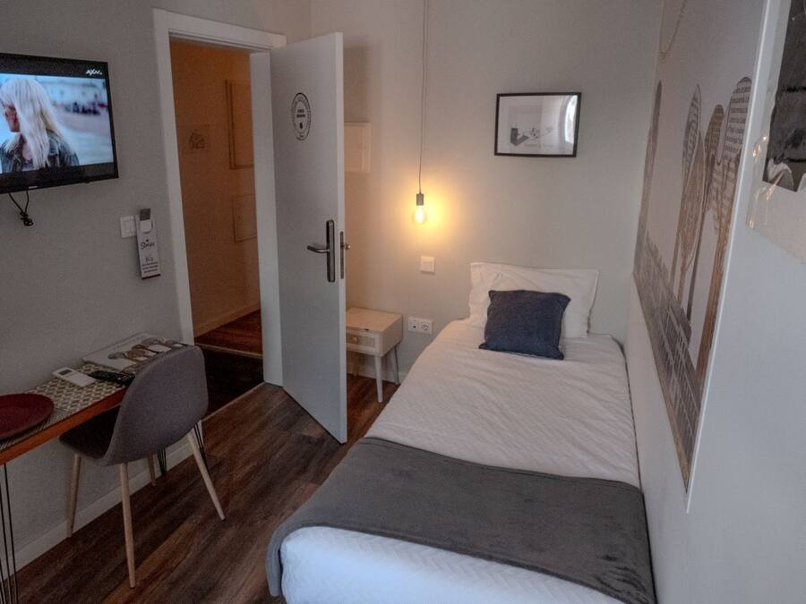 Una habitación pequeña y moderna con una cama, un escritorio y un televisor.