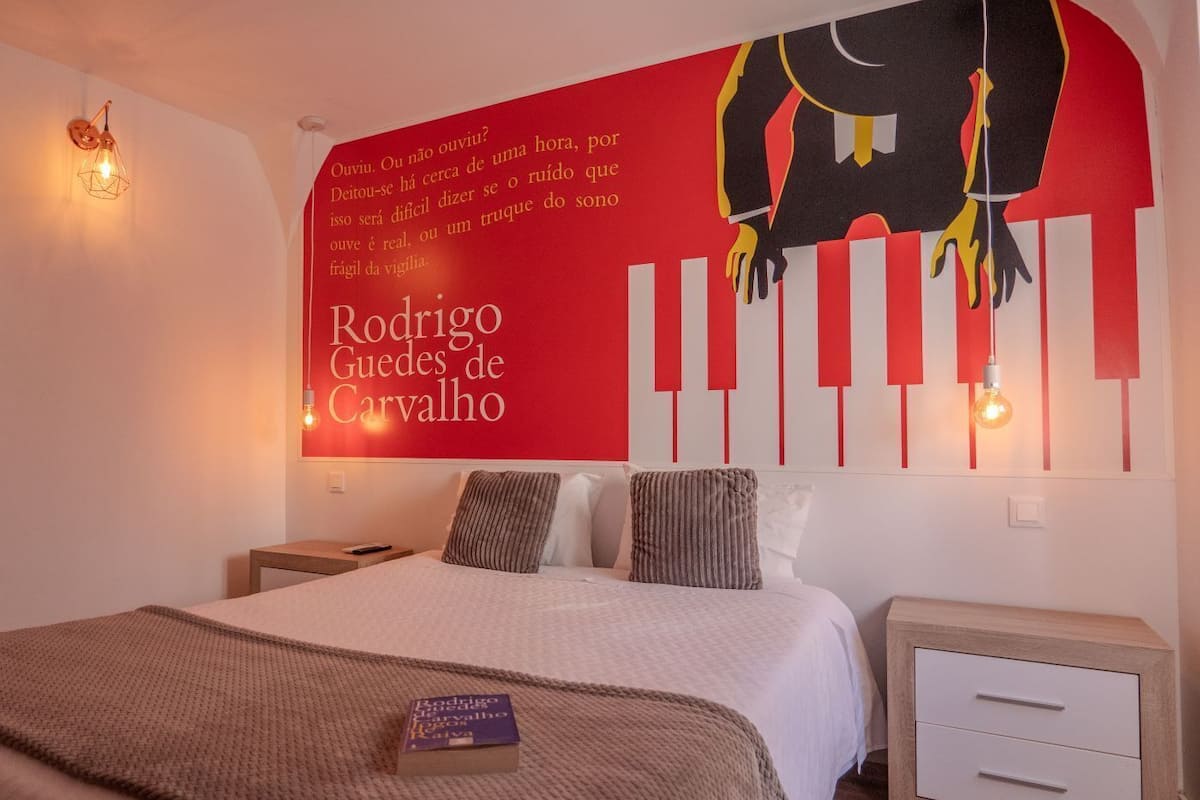 A bedroom with a bed, a nightstand, a wall with a red and black poster, and two wall-mounted lights.