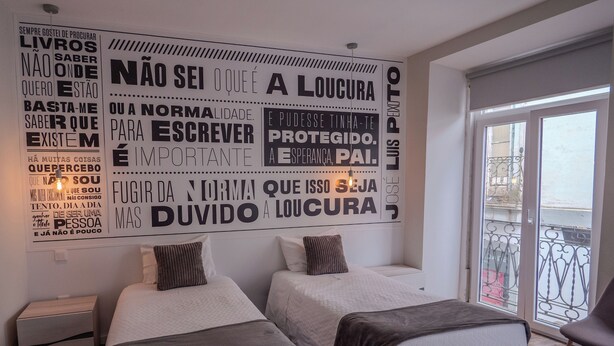 A hotel room with two beds, a large motivational wall, and a balcony with a metal railing. - Guest House Stories (Beja)
