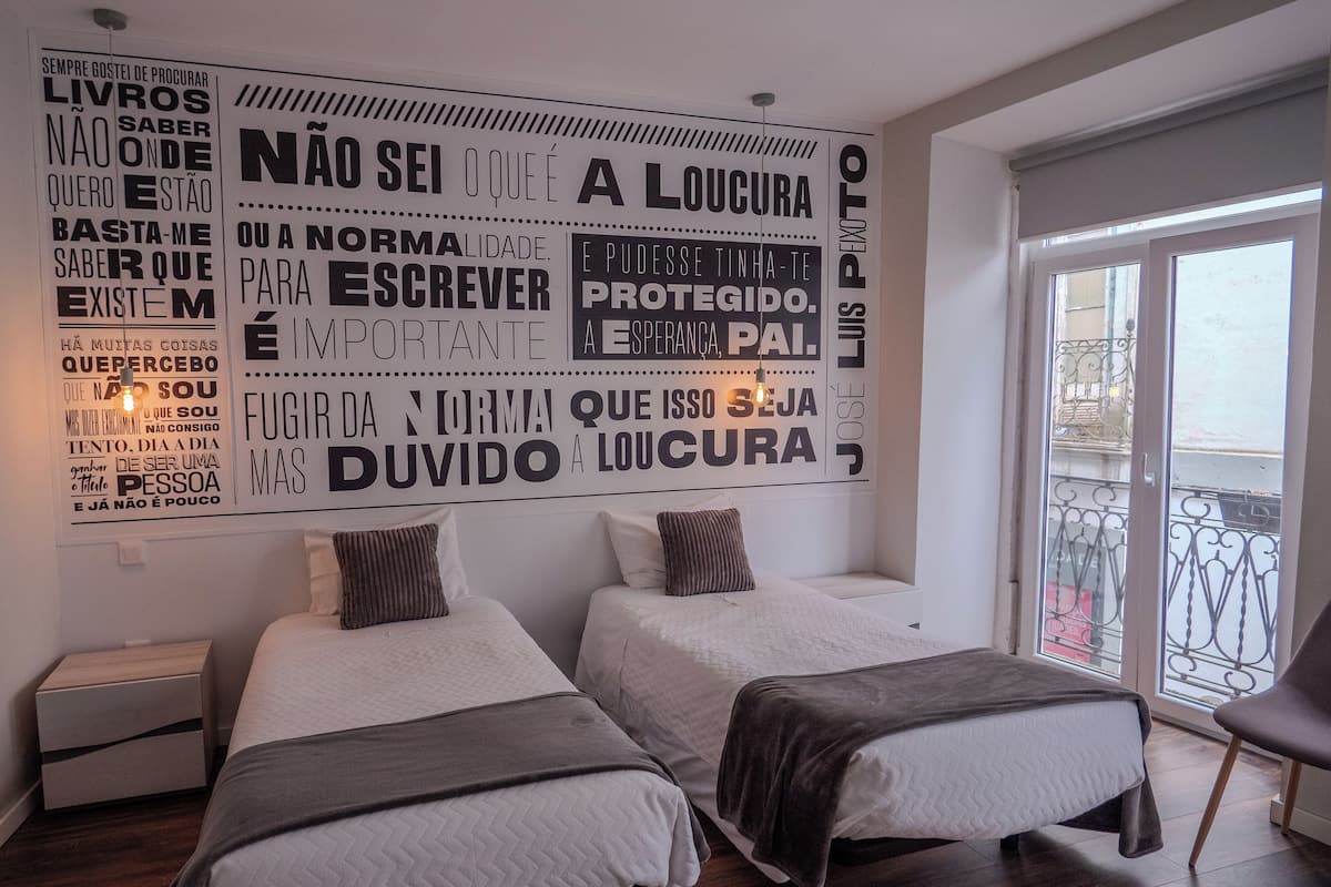 A hotel room with two beds, a large motivational wall, and a balcony with a metal railing.