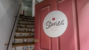 A red door with a circular sign that reads "Stories Suites & Breakfast" and a staircase with patterned tiles. - Guest House Stories (Beja)
