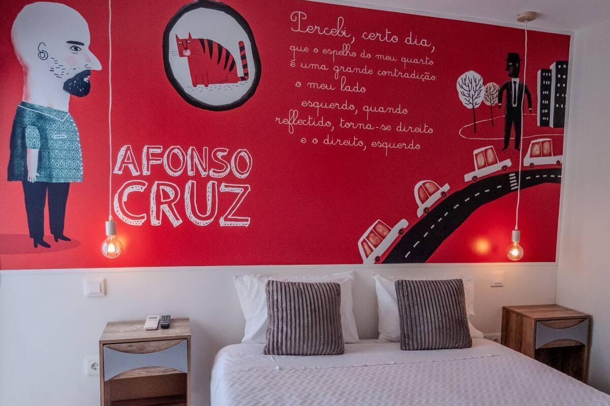 A bedroom with a large wall mural, a bed with gray and white bedding, two bedside tables, and a nightstand.
