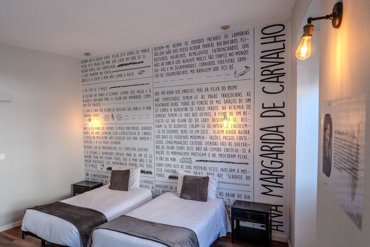 A hotel room with two beds, a large wall with text, and a wall-mounted light fixture.