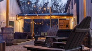 An outdoor seating area with Adirondack chairs, a fire pit, and a covered patio with string lights. - Modern Barndo, Hot Tub, Sauna, Fire Pit, 20 min RRG, Rec Room, Pickleball (Powell County)