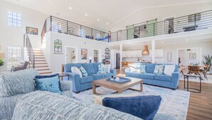 A spacious living area with two blue sofas, a wooden coffee table, and a staircase leading to a second floor. - Modern Barndo, Hot Tub, Sauna, Fire Pit, 20 min RRG, Rec Room, Pickleball (Powell County)
