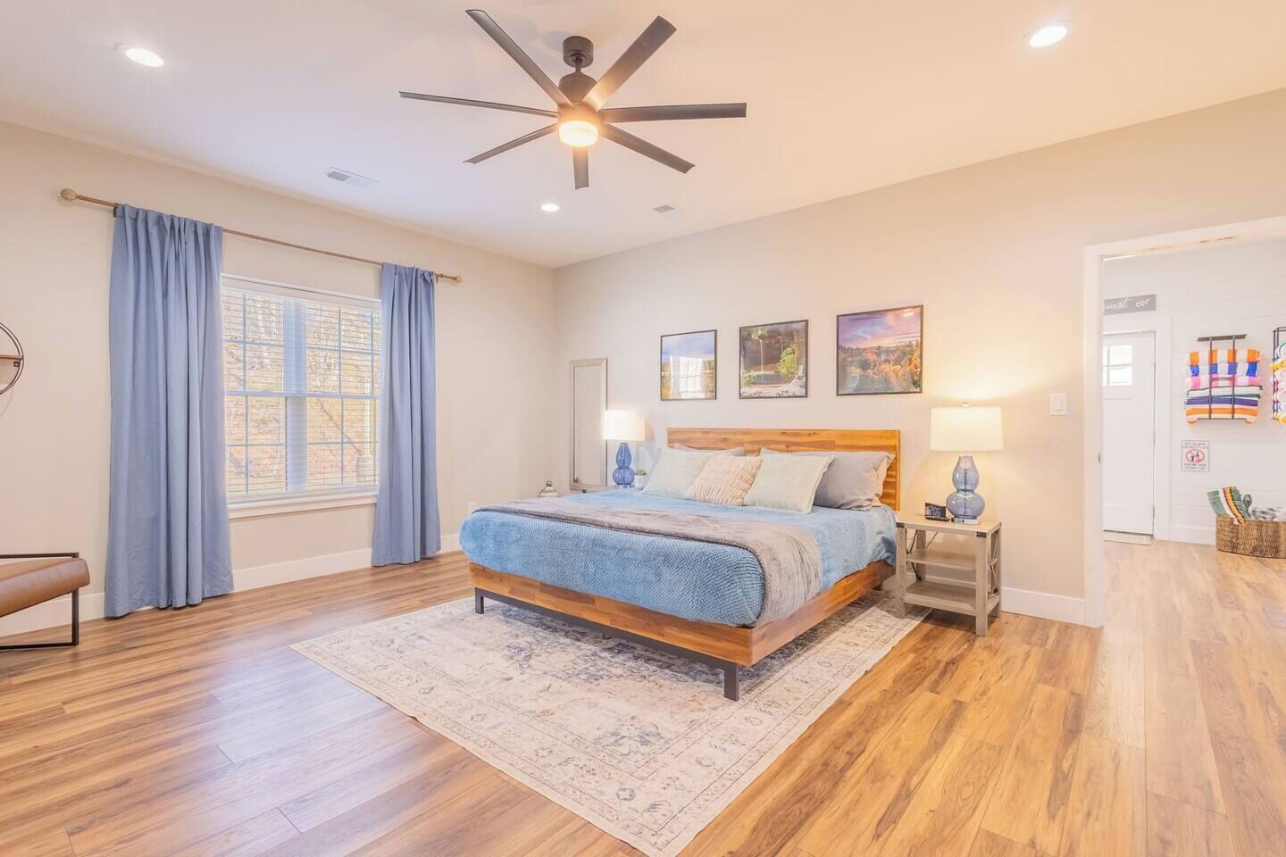 Une chambre à coucher comprenant un lit, un ventilateur de plafond, une fenêtre avec des rideaux et une porte donnant sur une autre pièce.