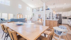 Amplia sala de estar con una mesa de comedor de madera, sofás azules y una cocina con alacenas blancas y electrodomésticos de acero inoxidable.