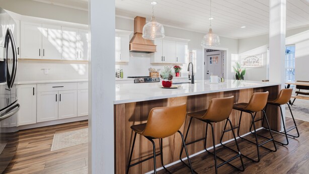 A modern kitchen with white cabinetry, a central island with bar stools, pendant lighting, and a visible stove. - Modern Barndo, Hot Tub, Sauna, Fire Pit, 20 min RRG, Rec Room, Pickleball (Powell County)