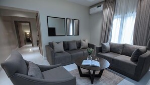 A modern living room with a grey sofa set, a coffee table with a book and vase, and a large mirror on the wall. - Dejays Homes and Shortlets (Abuja)