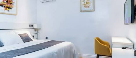 A hotel room with a bed, a desk, and a chair. There are two framed pictures on the wall.