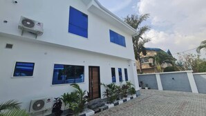 A two-story building with a white facade, blue-framed windows, and a central entrance. - Dejays Homes and Shortlets (Abuja)