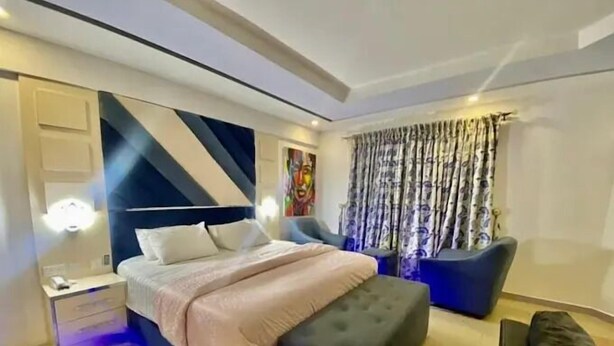 A modern bedroom with a bed, bedside table, and a chair. - Dejays Homes and Shortlets (Abuja)