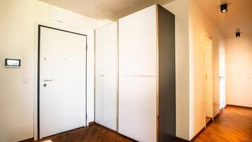 Un pasillo con una puerta blanca, un armario con puerta corredera de vidrio y suelo de madera.