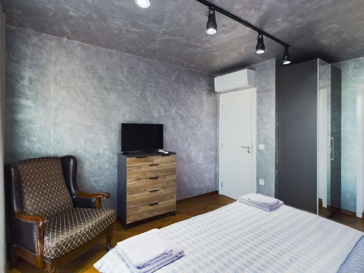 Ein Schlafzimmer mit einem Bett, einem Fernseher auf einer Holzkommode, einem Sessel und einem Kleiderschrank.