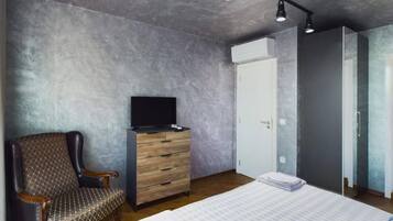 Ein Schlafzimmer mit einem Bett, einem Fernseher auf einer Holzkommode, einem Sessel und einem Kleiderschrank.