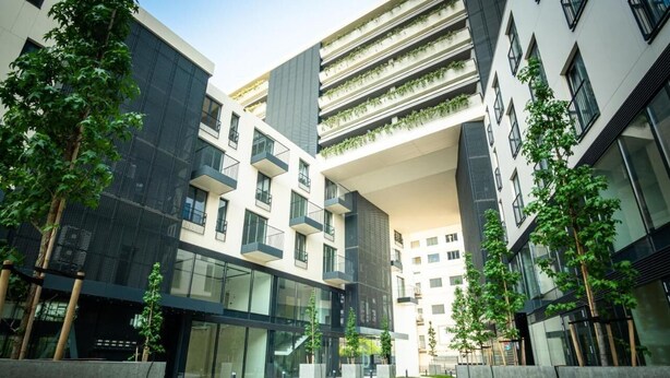 Een modern gebouw met meerdere verdiepingen, grote ramen en een centrale binnentuin met bomen en planten.