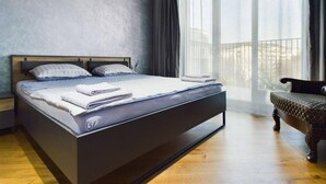 Een moderne slaapkamer met een groot bed, een houten vloer en uitzicht op de omgeving door een groot raam.
