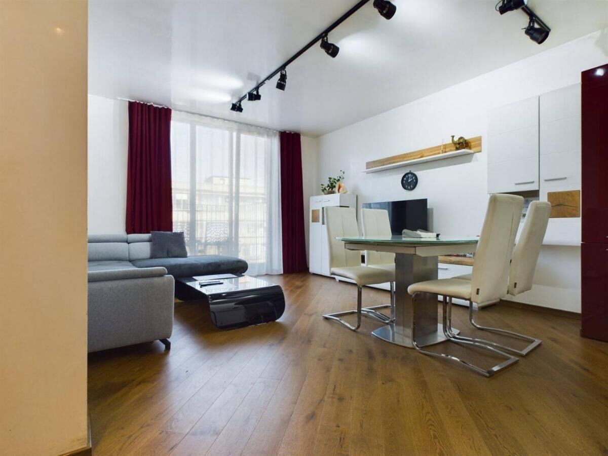Una sala de estar moderna con un sofá gris, una mesa de centro de vidrio y un comedor con una mesa blanca y dos sillas.