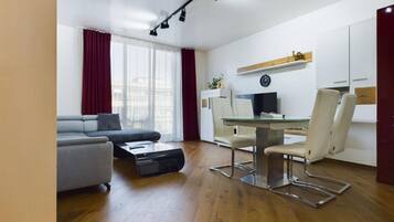 Una sala de estar moderna con un sofá gris, una mesa de centro de vidrio y un comedor con una mesa blanca y dos sillas.