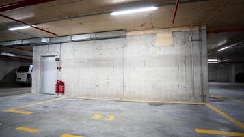 Ett parkeringsgarage med betongväggar, en vit skåpbil parkerad nära en utgång och brandsläckare monterade på väggen.