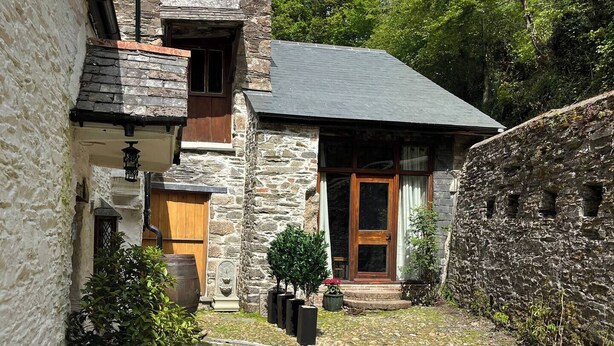 Ein Steinhaus mit Innenhof, mit einer Steinmauer, einer Holztür und einem kleinen Garten mit Blumen.