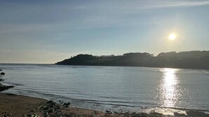 Ein Strand mit ruhigem Wasser, einer felsigen Küstenlinie und einer entfernten Hügelkette mit Bäumen.