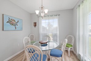 A dining area with a round glass table, white chairs, and a ceiling light fixture. - ⛱️Dog Friendly-Close to Beach-Seaside Solace⛱️ (Destin)