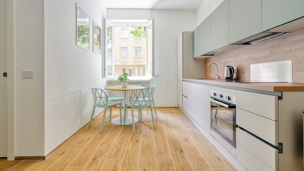 A modern kitchen with a wooden floor, white cabinets, and a dining area with a table and chairs. - Bright 1-br apartment in Porta Genova (Milan)