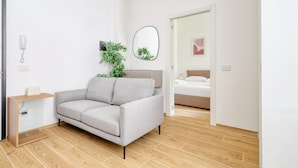 A modern living room with a grey sofa, a wooden console table, a potted plant, and a mirror on the wall. - Bright 1-br apartment in Porta Genova (Milan)