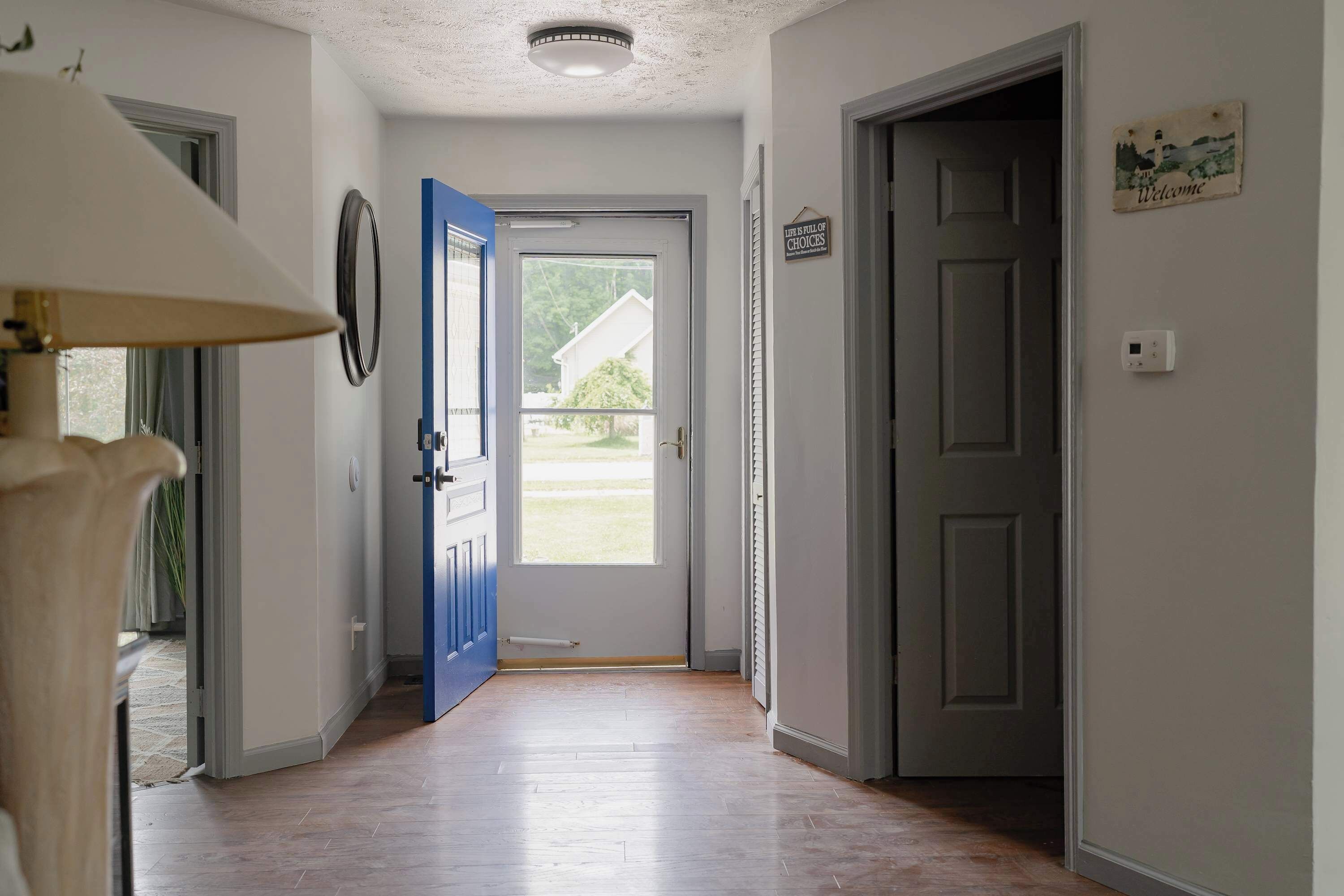 A hallway with a wooden floor, a blue door, and a welcome sign on the wall.