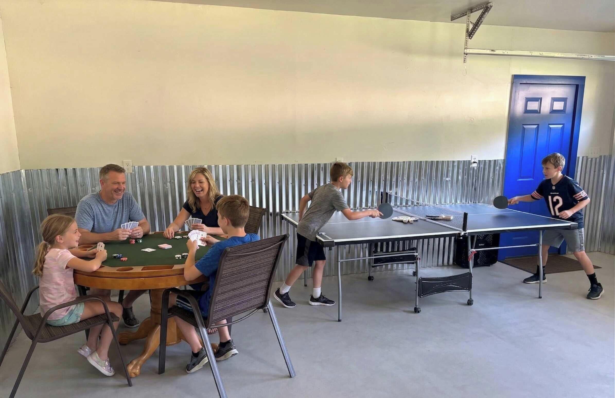 Een groep mensen speelt kaartspelletjes en tenniskegels in een ruimte met een golfblikken wand en een blauwe deur.