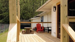 Une terrasse en bois avec une table et des chaises, un banc en pierre et une chaise rouge.