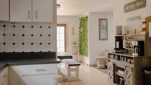 Une cuisine avec des meubles blancs, un banc en bois, une plante suspendue et un coin bar à café.