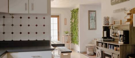 A kitchen with white cabinets, a wooden bench, a hanging plant, and a coffee bar area.