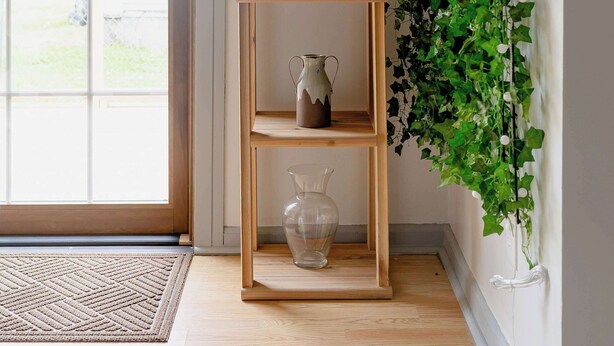 Une étagère en bois ornée d’objets décoratifs et d’une plante en pot, le tout adossé à un mur décoré de lierre vert.