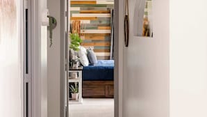 Un couloir mène à une chambre où se trouvent un lit, une plante et un miroir accroché au mur.