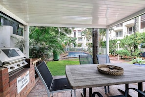 Un patio couvert avec un barbecue, une table et des chaises.