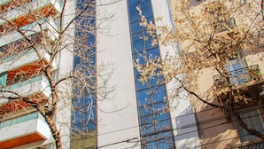 A modern building with a large glass facade, a tree in front, and a clear blue sky. - Telepostal Congreso (Buenos Aires)