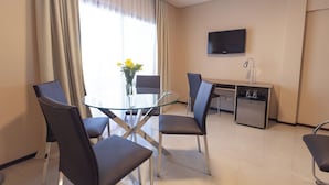 A modern hotel room with a glass dining table, four chairs, a small desk with a TV, and a minibar. - Telepostal Congreso (Buenos Aires)