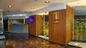 A hotel reception area with a wooden reception desk, a television screen, and a bamboo plant display. - Telepostal Congreso (Buenos Aires)