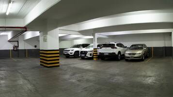 Un aparcamiento con varios coches estacionados en plazas delimitadas, un extintor en la pared y un bolardo con rayas amarillas y negras.