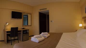 A hotel room with a bed, a desk, a chair, a TV, and two towels on the bed.
