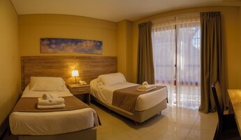 Habitación de hotel con dos camas, cabecero de madera, mesita de noche con lámpara, teléfono y un cuadro en la pared.