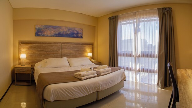A hotel room with a large bed, two bedside lamps, a painting on the wall, and a view through sheer curtains. - Telepostal Congreso (Buenos Aires)